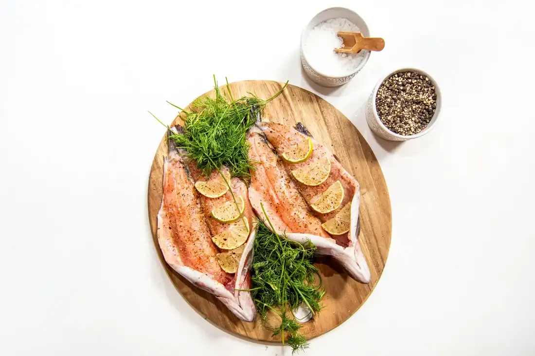 Whole trout dressed with lemon and dill on a wooden board